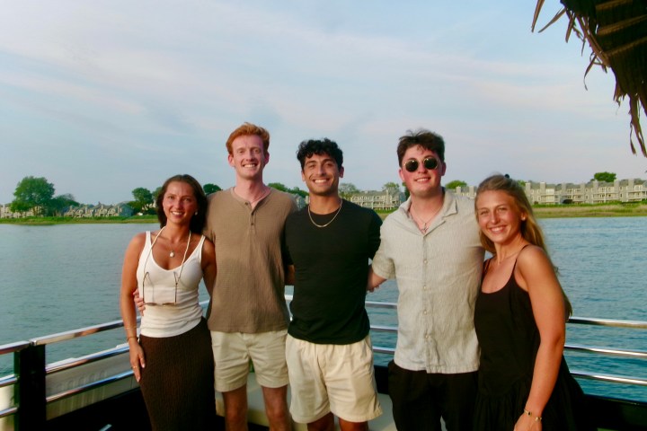 Five people posing on a boat with a waterfront view.