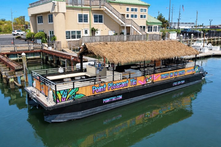Tiki boat with colorful designs docked near a riverside building.