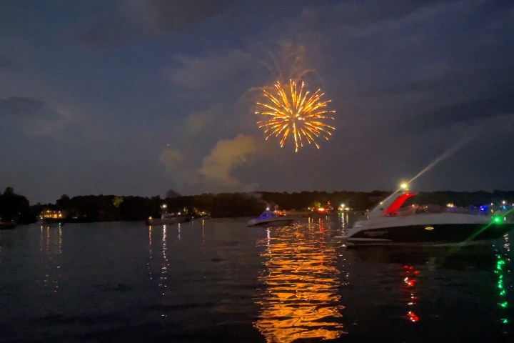 Fireworks above a lake with boats at night, reflecting on the water.