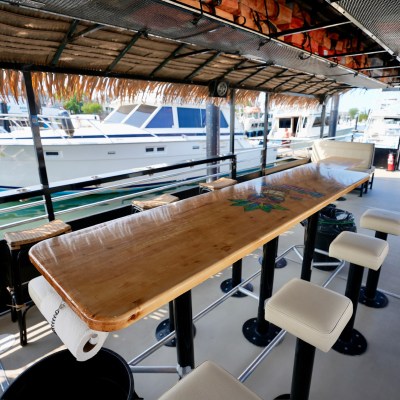 Boat deck with long table, stools, and view of docked yachts in marina.