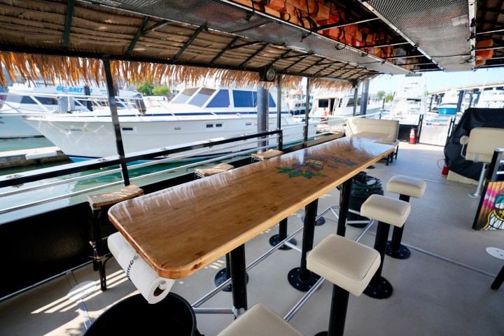 Boat docked with a bar setup, stools, and tropical decor, overlooking other boats and marina.