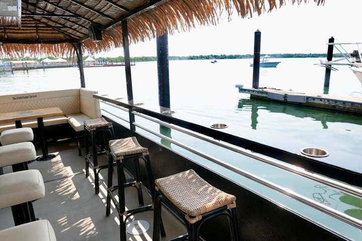 Boat with straw roof, bar stools, and lake view in background.
