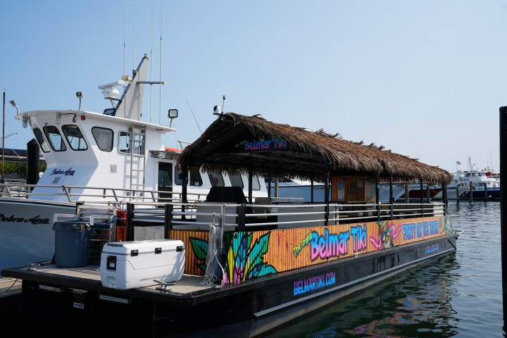Tiki-themed boat with straw roof and colorful decorations docked next to white boat in marina.