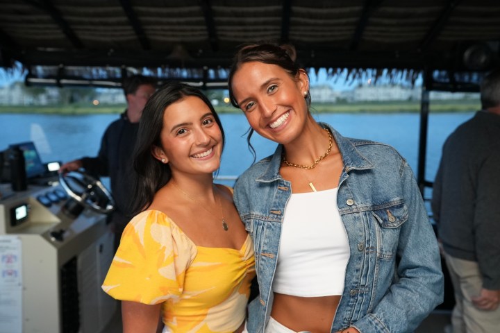 Two smiling women on a boat, one in a yellow dress, the other in a denim jacket, posing for a photo.