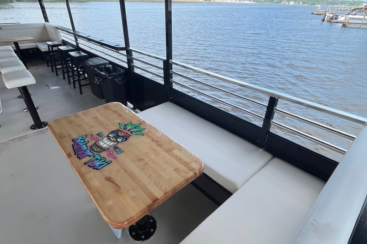 Tiki boat with seating area and a wooden table, overlooking a calm body of water.