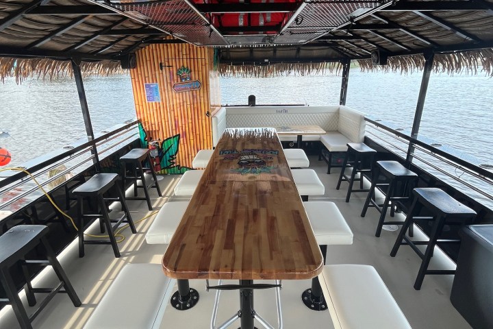 Boat interior with a long table, chairs, life jackets overhead, and lake view.