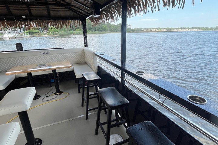Boat with bar stools and thatched roof on calm water.
