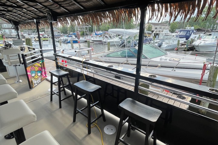 Boat deck with bar stools, tiki-style roof, and marina view with several docked boats.
