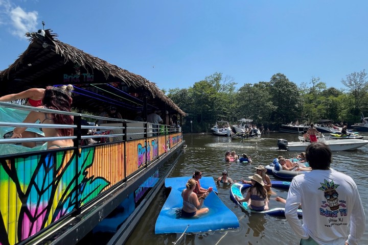 People relaxing on a floating mat next to a colorful boat under a clear blue sky.