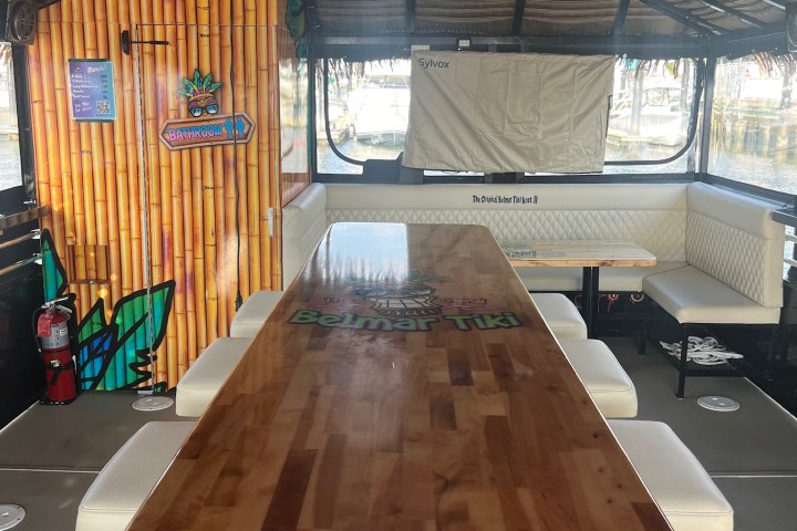 Interior of a tiki-style boat with wooden table, cushioned benches, and life jackets overhead.