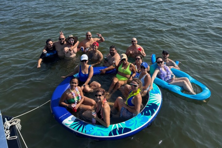Group of people on inflatable rafts in water, smiling and holding drinks.