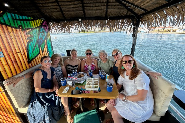 Seven women smiling at a table on a boat with water in the background.