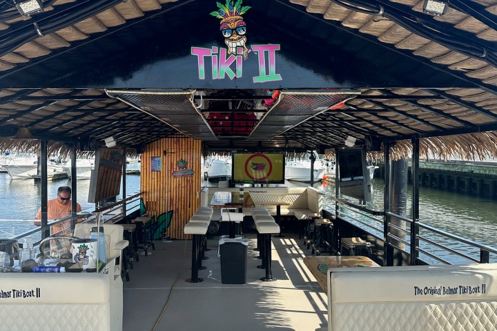 Interior of a tiki boat with palm-thatched roof, tables, and banquette seating.