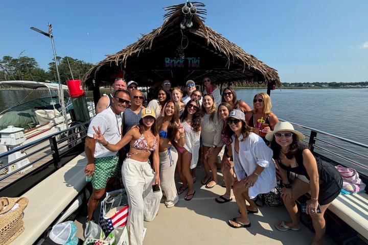 Group of people smiling on a boat with a tiki hut roof, surrounded by water.