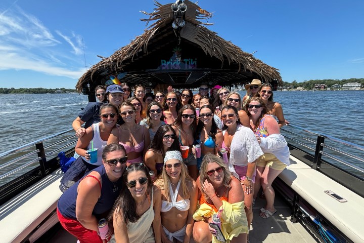 Large group of people posing on a tiki boat under clear blue sky.