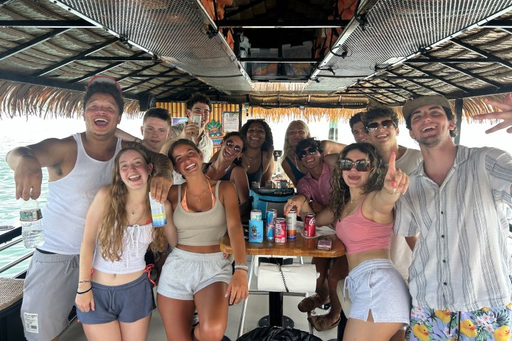 Group of people smiling and posing on a boat with drinks.