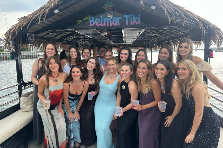 Group of smiling people posing on a tiki boat with 'Belmar Tiki' sign above.