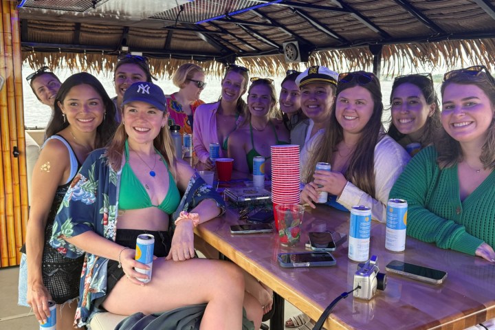 Group of people smiling, sitting around a tiki bar with drinks on a boat.