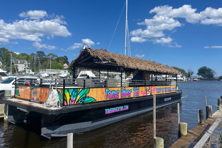 Colorful tiki-themed boat at dock under clear blue sky with scattered clouds.