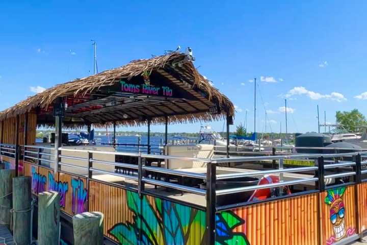 Tiki boat with thatched roof docked at a marina under a clear blue sky.
