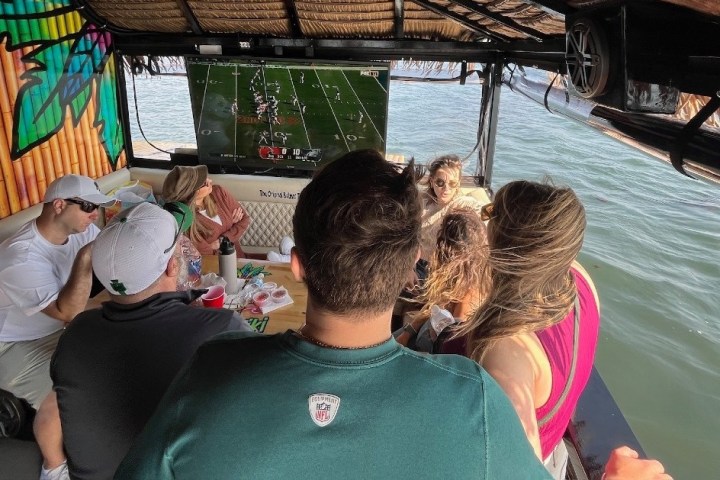 Group of people on a boat watching a football game on a TV.