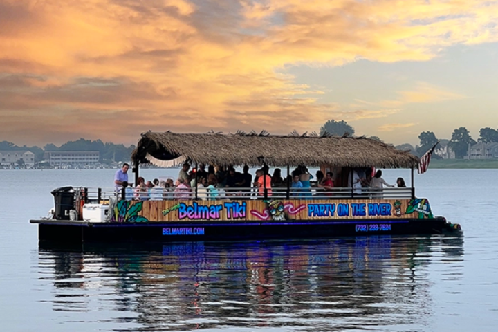 People on a tiki bar boat on a lake at sunset.