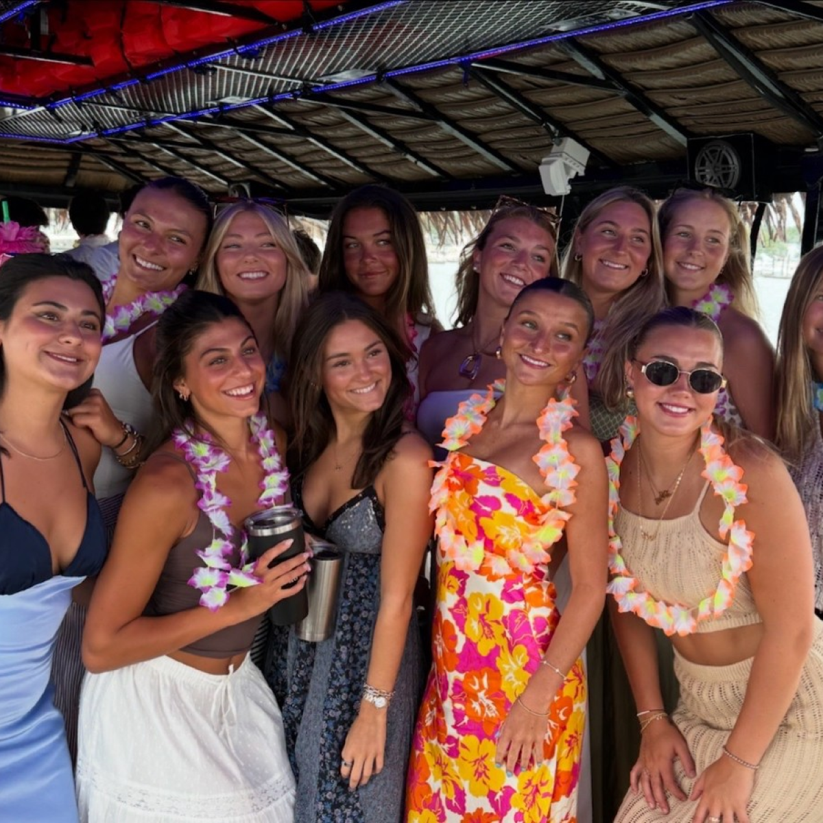 Group of smiling women on a boat, wearing colorful dresses and leis.