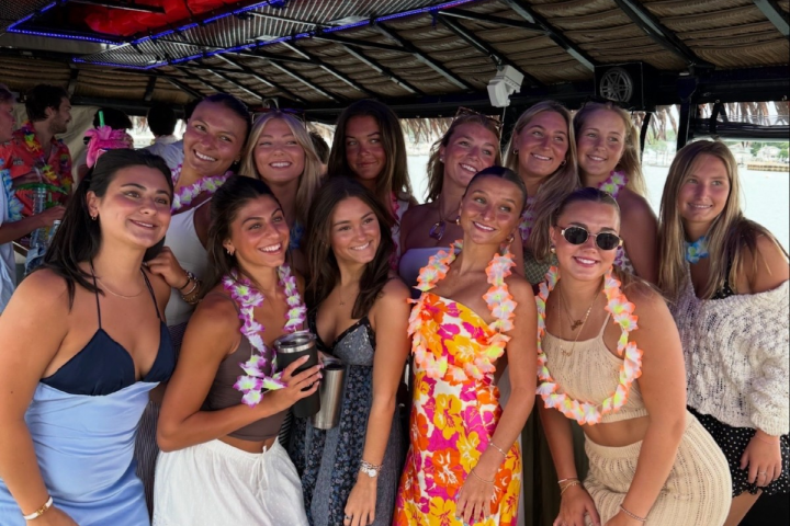 Group of smiling women on a boat, wearing colorful dresses and leis.