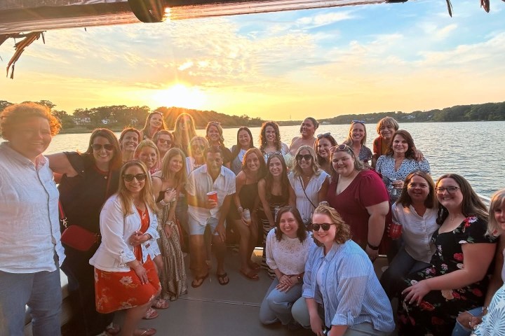 A group of people posing on a boat at sunset with a lake and trees in the background.