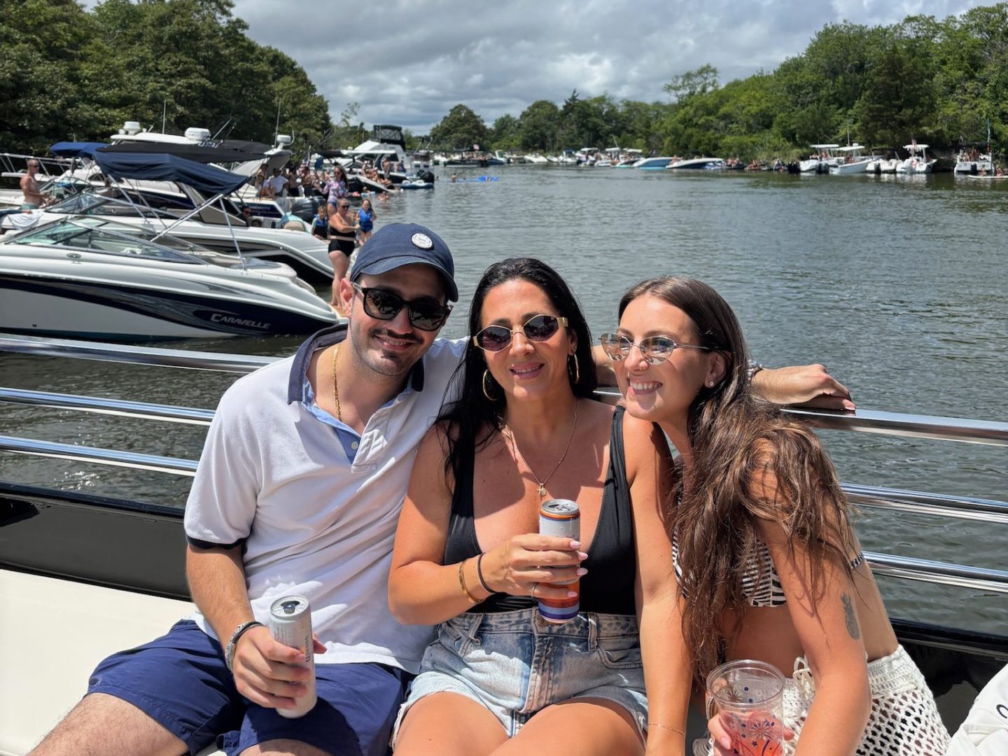 Three people smiling on a boat with drinks, surrounded by water and trees.