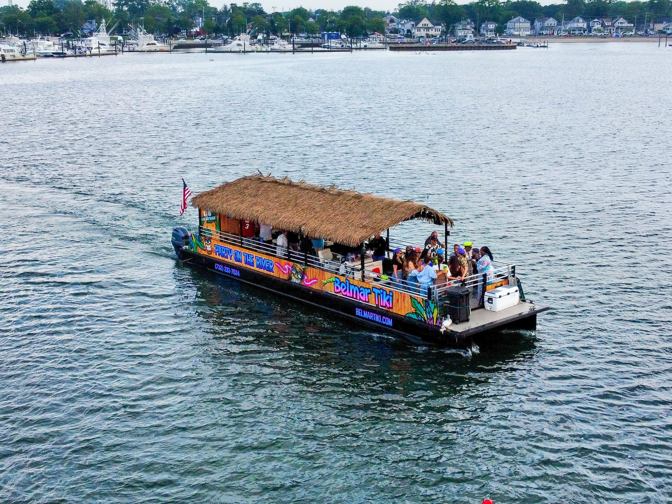 Tiki-themed boat with passengers cruising on a lake near a marina.