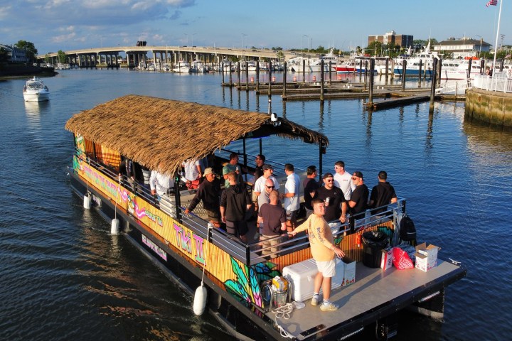 Group of people on a boat with a thatched roof sailing in a marina.