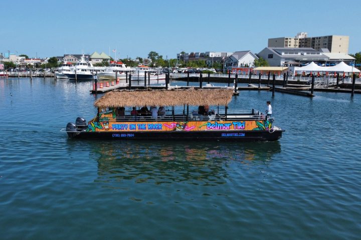 Colorful tiki boat on a river with marina and buildings in the background under a clear sky.