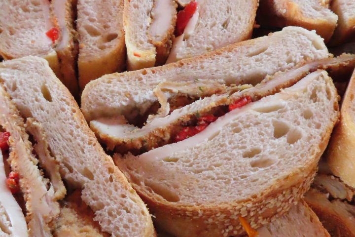 Stack of sliced sandwiches with turkey and red peppers on a wooden board.