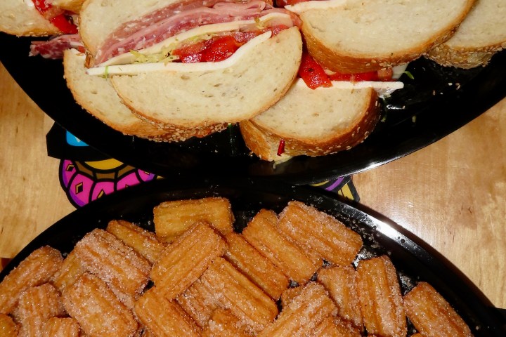 Plates with sandwiches of meat and red peppers and churros on a wooden table.