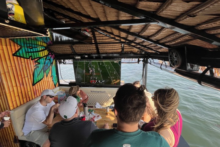 People on a boat watching football on a TV, surrounded by water.