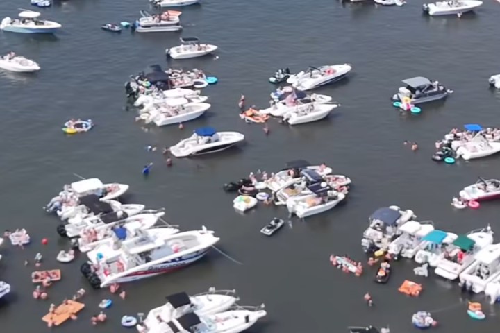 Aerial view of many boats clustered on a lake with people swimming and using floaties.
