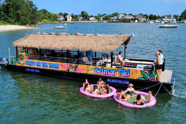 People on a tiki boat and in pink floats on a sunny river.