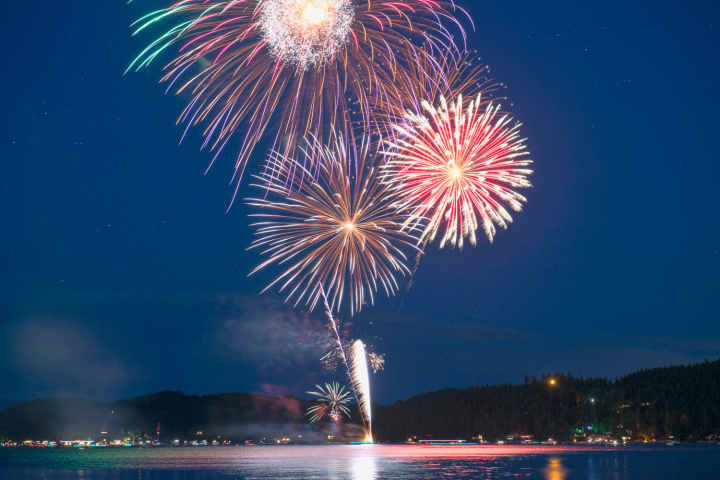 Colorful fireworks bursting over a calm lake at night with a dark, clear sky.