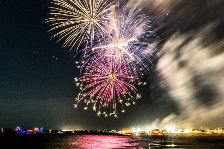Colorful fireworks exploding over a beach at night with reflections on the water.
