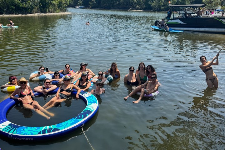 Group of people relaxing in a river with floats and a boat nearby.