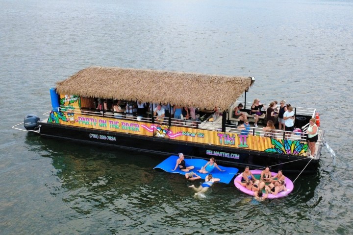 People on a tiki bar boat and floating mats in a lake.