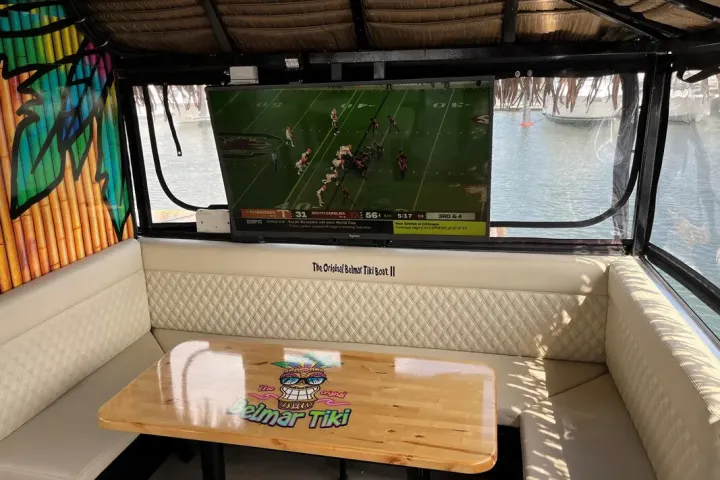 Outdoor seating with a TV showing a football game, beside a water view.